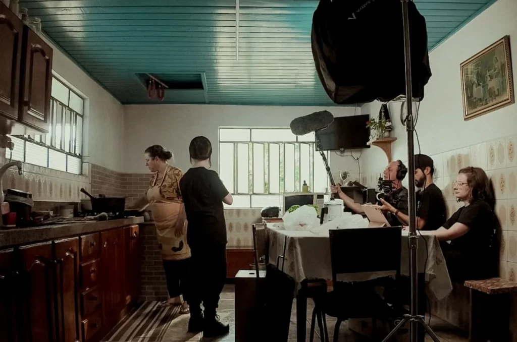 Bastidores das gravações do curta-metragem "Nos Tempos da Nonna", mostrando o elenco e a equipe técnica em um cenário típico de colônia italiana