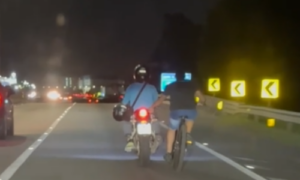 Ciclista é transportado por motociclista em rodovia