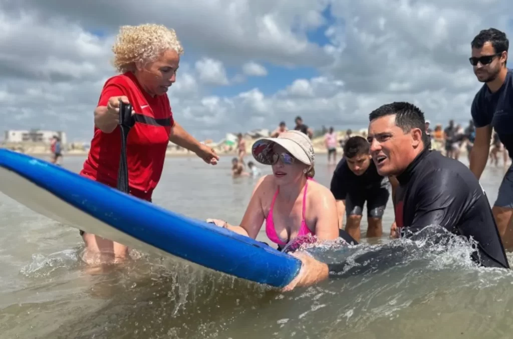 Imagem de participantes do projeto Abba Surf desfrutando de atividades aquáticas inclusivas na orla do Balneário Rincão, com instrutores e voluntários auxiliando pessoas com deficiência em pranchas de stand-up paddle, promovendo lazer e inclusão social